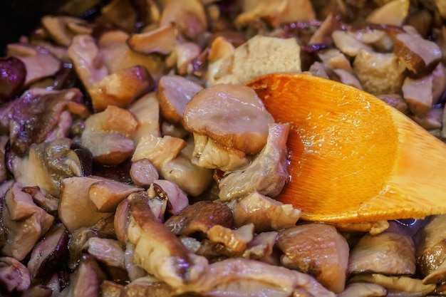 Champignons worden gebakken in koekenpan Close-up Heerlijk gerecht van verse champignons Houten lepel interfereren met champignons