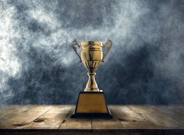 Photo champion golden trophy placed on a wooden table with dark and smoke background