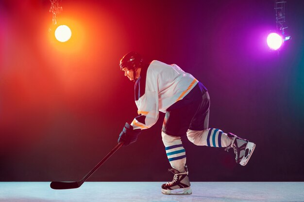 Champion. Male hockey player on ice court and dark neon colored background with flashlights. Sportsman in equipment, helmet practicing. Concept of sport, healthy lifestyle, motion, wellness, action.