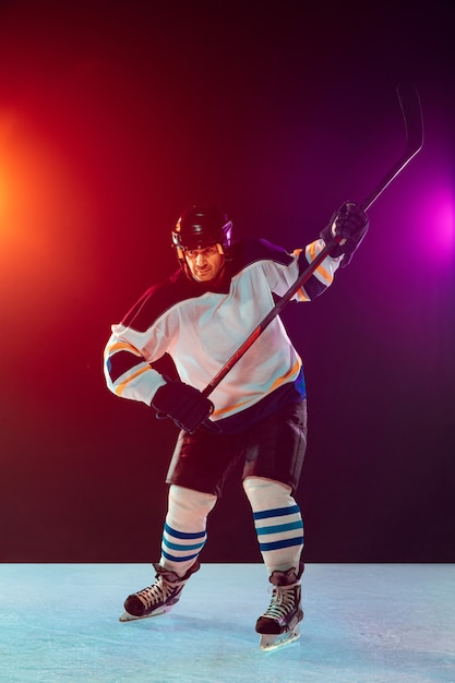 Champion. Male hockey player on ice court and dark neon colored background with flashlights. Sportsman in equipment, helmet practicing. Concept of sport, healthy lifestyle, motion, wellness, action.