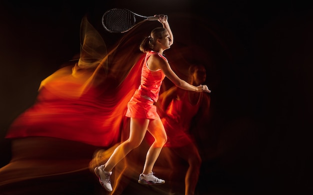 チャンピオン。混合光の中で黒いスタジオの背景に分離されたプロの女子テニス選手のトレーニング。スポーツスーツの練習の女性。健康的なライフスタイル、スポーツ、トレーニング、モーション、アクションのコンセプト。