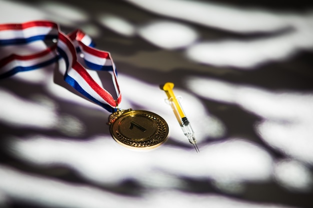 Champion's gouden medaille en spuit met dopingsubstantie met lichten en schaduwen die door het raam komen. Sport- en dopingconcept