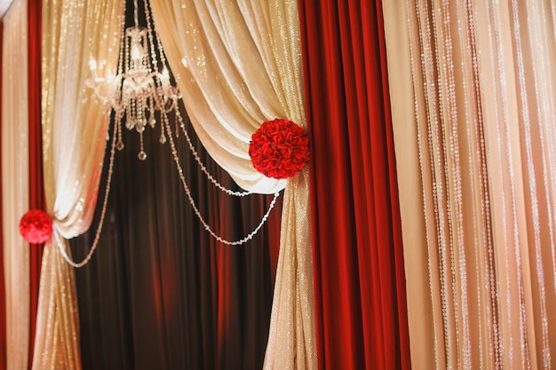 A chandelier hangs from the ceiling with red and white curtains.