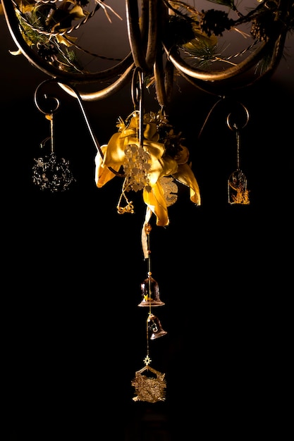 Chandelier with golden Christmas ornaments with bells and bows on dark background