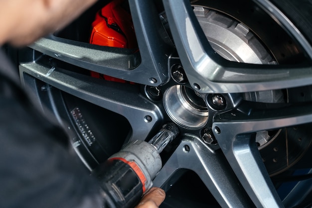 Changing car wheel in auto repair shop using an electric drill to loosen the bolts concept of