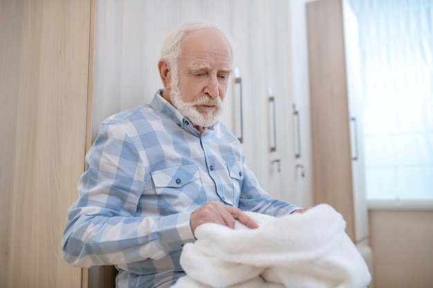 Changing room. Gray-haired mature man in a changing room in spa center with towels in hands