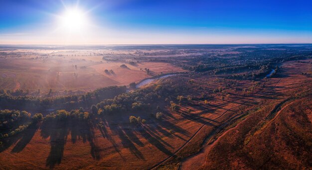 The channel and bends of the river on a marshy meadow Orange dry grass scorched by the summer heat and morning fog A wonderful landscape at dawn Drone view