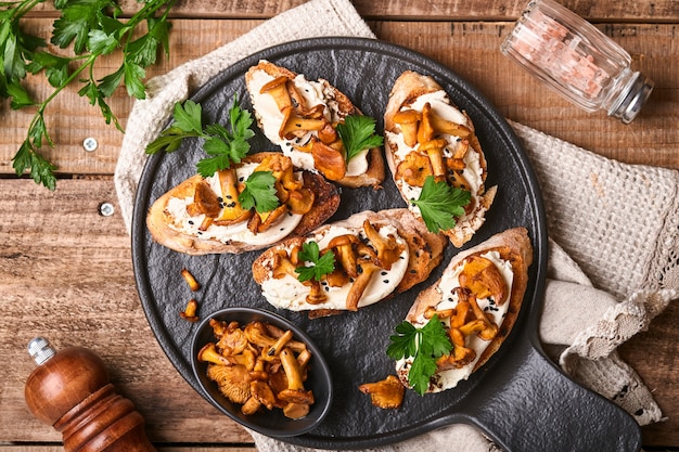 Chanterelle sandwiches with cheese. Open faced sandwich with creamy cheese, seasonings and pepper and fresh parsley on an old wooden background. Mock up. Top view.