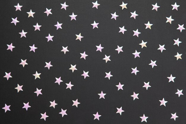 Chaotisch patroon van talrijke parelconfettien in vorm van kleine sterren op zwarte papierachtergrond. Viering, vakantie, verkoop, mode