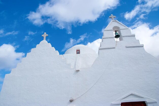 Chapel building detail in Mykonos, Greece. Church dome and croses architecture. White church on cloudy blue sky. Religion and cult concept. Summer vacation on mediterranean island.