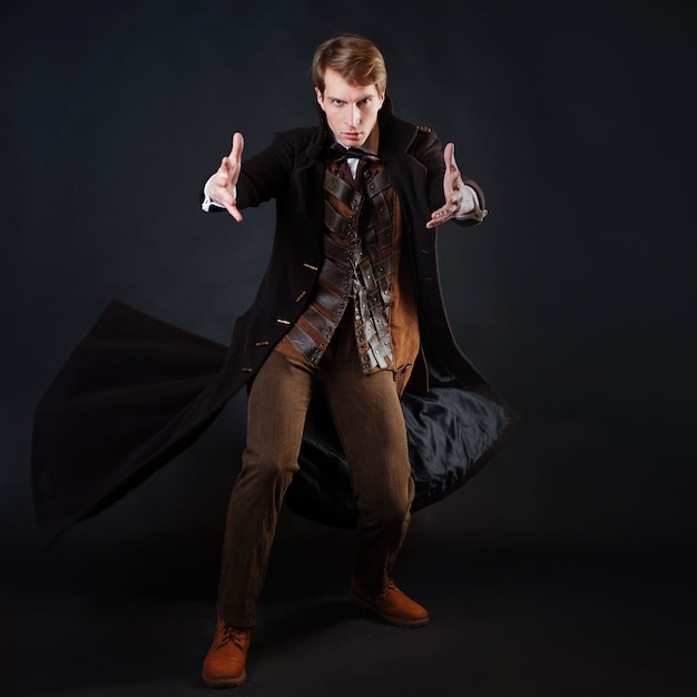 Photo character of steampunk story, young attractive man in an elegant long coat, adventurer makes an epic gesture. intelligent gentleman in victorian style. vintage retro suit, young attractive man