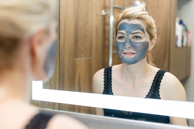 Maschera viso al carbone o fango di argilla nera. bella donna con maschera nera sul viso, primo piano colpo alla testa dello studio. concetto di cosmetici naturali.