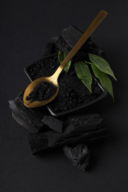 Charcoal powdered charcoal spoon and leaves on black background