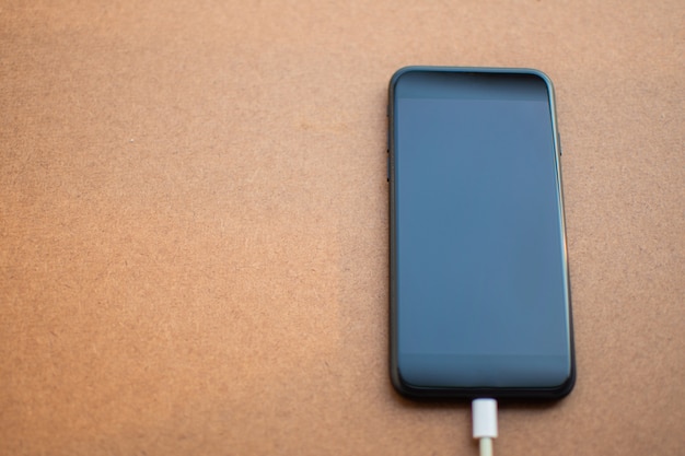 Charging battery mobile phone with blank screen on the wooden table. 