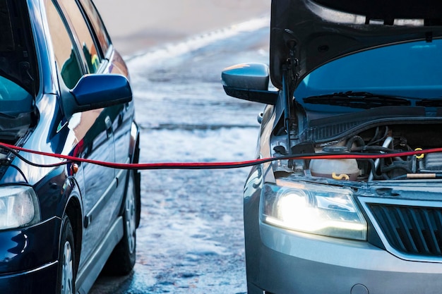 Charging a car battery in winter help on the road closeup\
connecting high voltage wires to the car battery resuscitation of\
the car in severe winter conditions