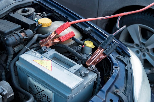 Charging a car battery in winter help on the road closeup\
connecting high voltage wires to the car battery resuscitation of\
the car in severe winter conditions