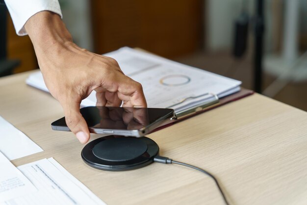 Charging mobile phone battery with wireless charging device in the table Smartphone charging on a charging pad Mobile phone near wireless charger Modern lifestyle technology concept