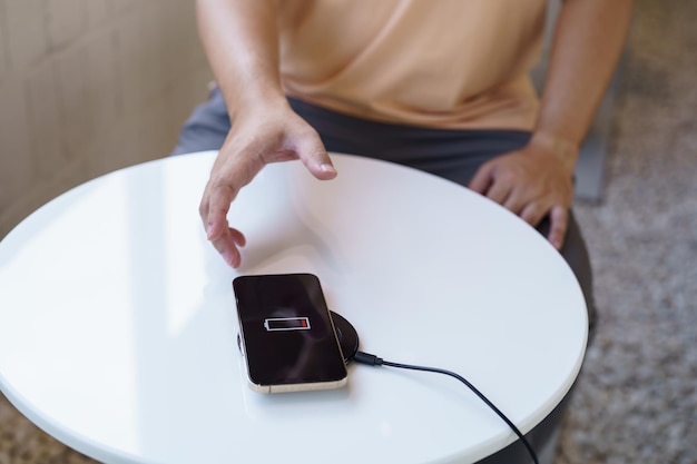 テーブルにあるワイヤレス充電デバイスで携帯電話のバッテリーを充電する 充電パッドで充電するスマートフォン ワイヤレス充電器の近くにある携帯電話 現代のライフスタイルテクノロジーのコンセプト