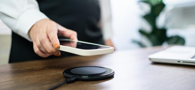 Charging mobile phone battery with wireless charging device in the table Smartphone charging on a charging pad Mobile phone near wireless charger Modern lifestyle technology