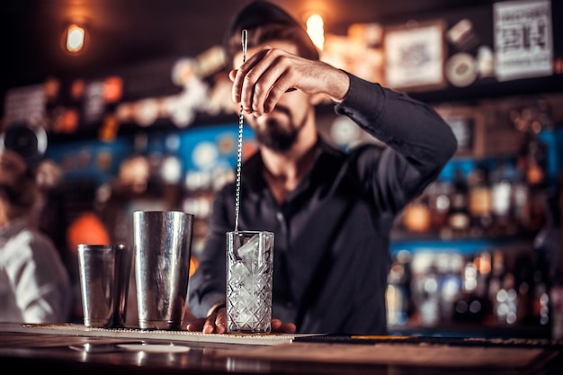 Charismatic bartender demonstrates the process of making a cocktail while standing near the bar counter in pub