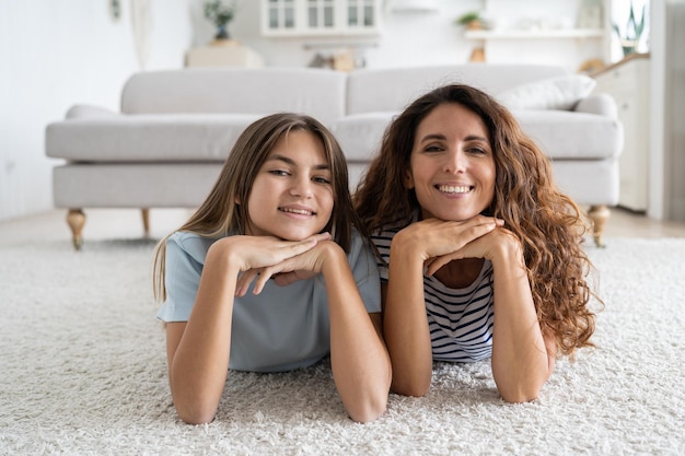 Charismatic cheerful woman and teen girl lying on floor with carpet posing for family photo