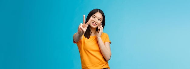 Charismatic cute girl share positive news talking smartphone\
show peace victory sign smiling satisfi