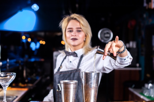 Charismatic girl barman places the finishing touches on a drink at the nightclub