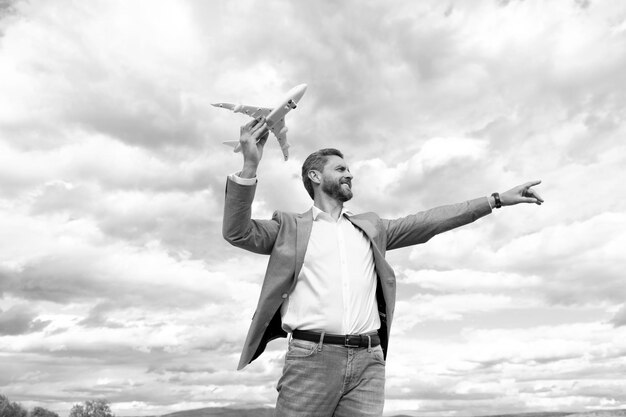 ジャケットのカリスマ的な幸せなビジネスマンは、空の背景のアイデアにおもちゃの飛行機を保持します