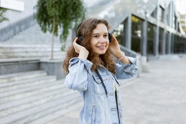 Charismatic middle aged curly hair cheerful woman listening to music on headphones in city