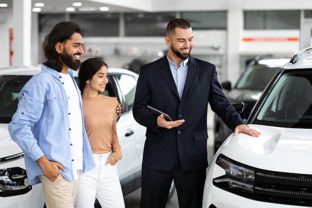 Charismatic salesman with tablet demonstrated luxury car features to couple