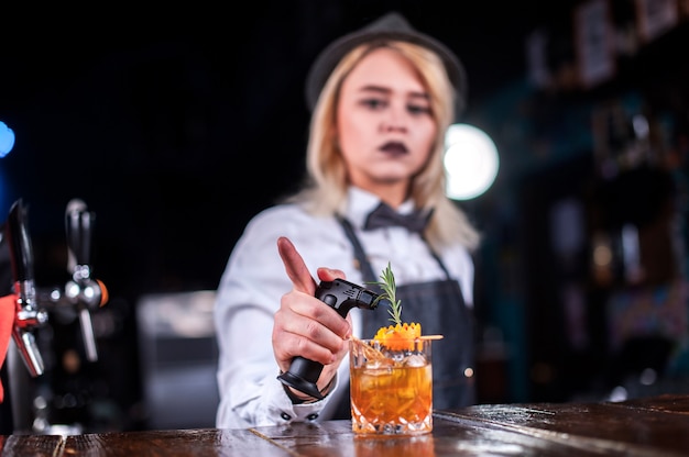 Charismatic woman bartender intensely finishes his creation while standing near the bar counter in bar