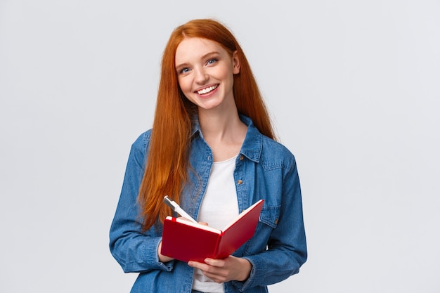 Charismatisch getalenteerde schattige roodharige vrouwelijke student studeert, notities maken na leraar in notitieblok