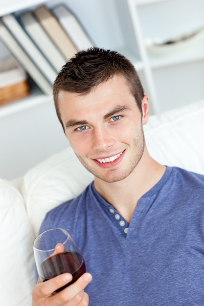 Foto charismatische jonge man met een glas wijn, zittend op een bank in de woonkamer