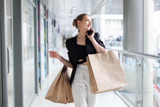 Charismatische jonge vrouw met boodschappentassen praten aan de telefoon in winkelcentrum