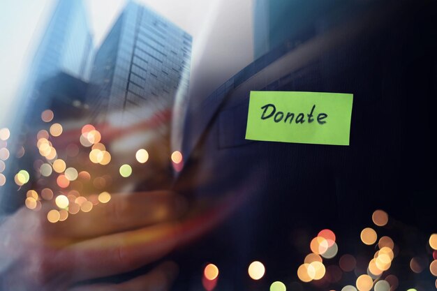 Charitatieve schenking in bedrijfsconcept Zakenman toont een papier met het woord doneren Dubbele blootstelling wolkenkrabber