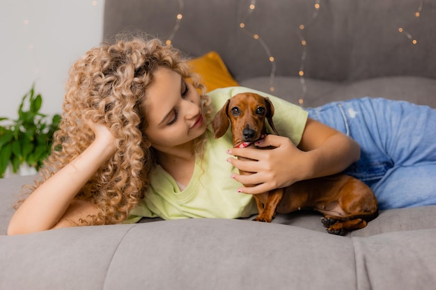 Charmant blond meisje met krullen ligt op een grijs bed met een teckelhond