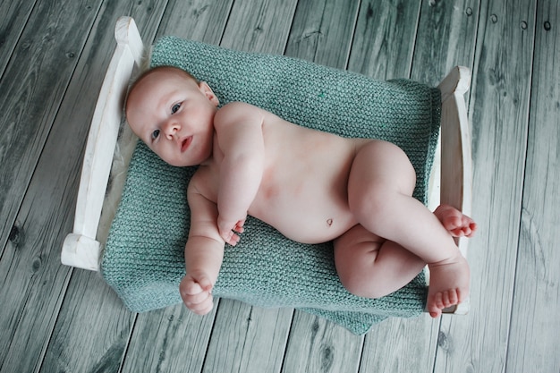 Charmant en lief een pasgeborene is bedekt met een gebreide deken in een met de hand gemaakt houten bed op het groene houten parket als achtergrond