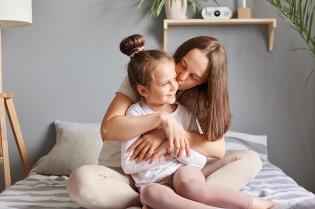 Charmant klein kindmeisje dat moeder feliciteert met moederdag dochter zittend in bed met mama zacht moment in de ochtend vrouw die haar kind met liefde kust