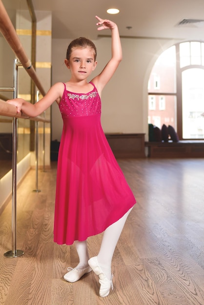 Foto charmant klein meisje droomt ervan ballerina te worden het meisje in de roze jurk danst terwijl ze zich vasthoudt aan de barbabymeisje studeert ballet