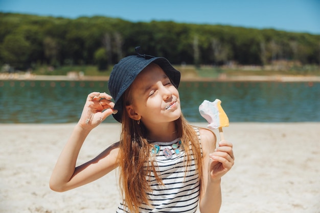 Charmant klein meisje in een hoed eet ijs op het strand van het strand Zomervakantie concept