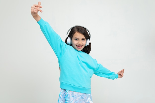 Charmant meisje in een turquoise blouse met een grote koptelefoon geniet van muziek en dansen