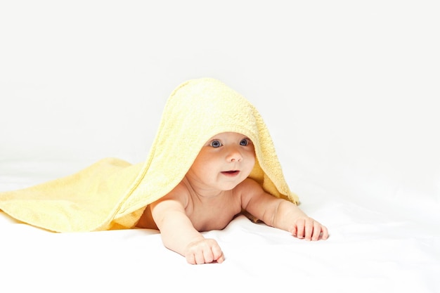 Charmant, schattig, gelukkig babymeisje met blauwe ogen in een gele handdoek op een witte achtergrond.