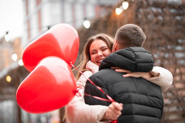 Foto charmant stel knuffelen op straat na een date. een jonge, mooie dame houdt hartvormige ballonnen in haar hand en lacht. valentijnsdag concept, geschenken, liefde