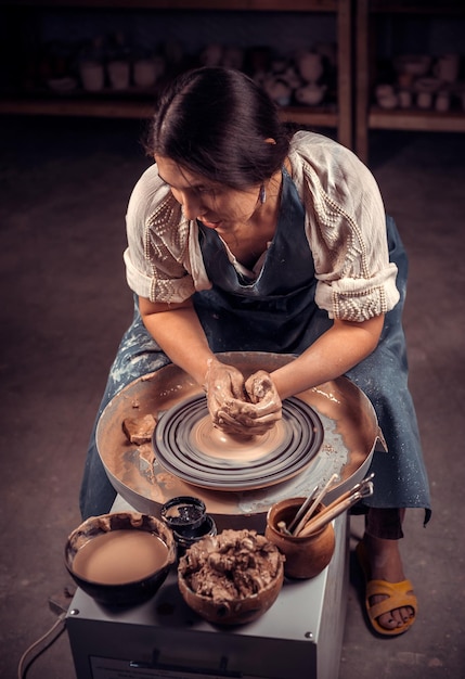 Charmante ambachtelijke meisjesbeeldhouwer werkt met klei op een pottenbakkersschijf en aan tafel met de gereedschappen. Ambachtelijke industrie.