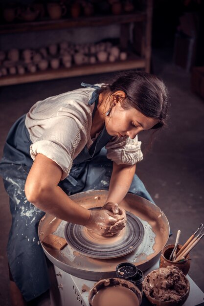 Charmante ambachtelijke vrouw maakt een nieuw aardewerk van klei op een pottenbakkersschijf.