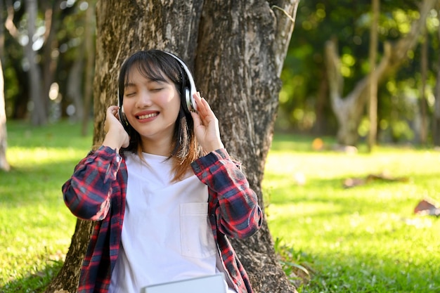 Charmante Aziatische vrouw die naar muziek luistert via haar koptelefoon terwijl ze in het park zit