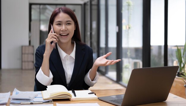 Charmante aziatische vrouw met een glimlach die papieren en mobiele telefoon op kantoor vasthoudt