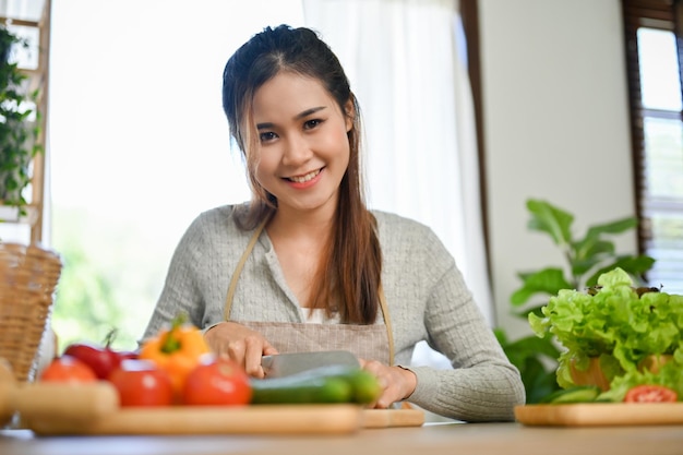 Charmante Aziatische vrouwelijke huisvrouw die komkommer hakt en het ingrediënt van haar eten klaarmaakt