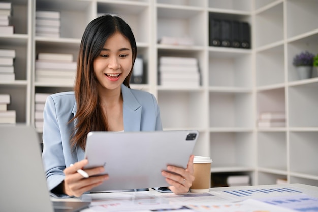 Charmante Aziatische zakenvrouw met behulp van haar digitale tablet aan haar bureau op kantoor