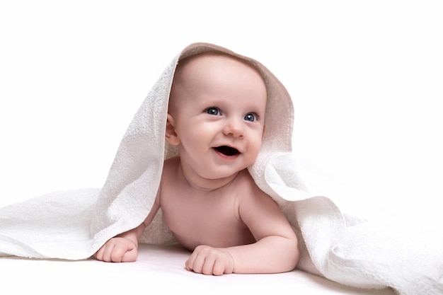 Charmante baby op een witte achtergrond onder een handdoek die met een glimlach naar de camera kijkt